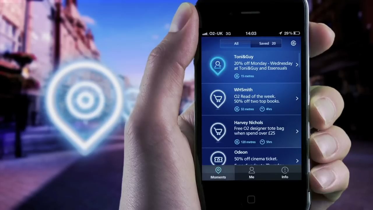 Frame from O2's 2011 launch film: a hand holds a phone on a high street showing the Priority Moments offers list — Toni&Guy 15 metres away, WHSmith 32 metres, Harvey Nichols 120 metres, Odeon below